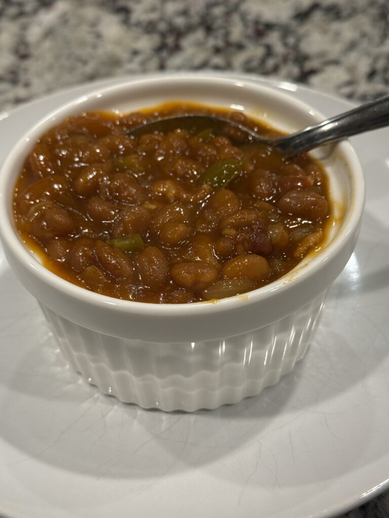 Baking dish filled with thick, bubbly Southern-style baked beans, topped with crispy bacon strips and garnished with chopped parsley.