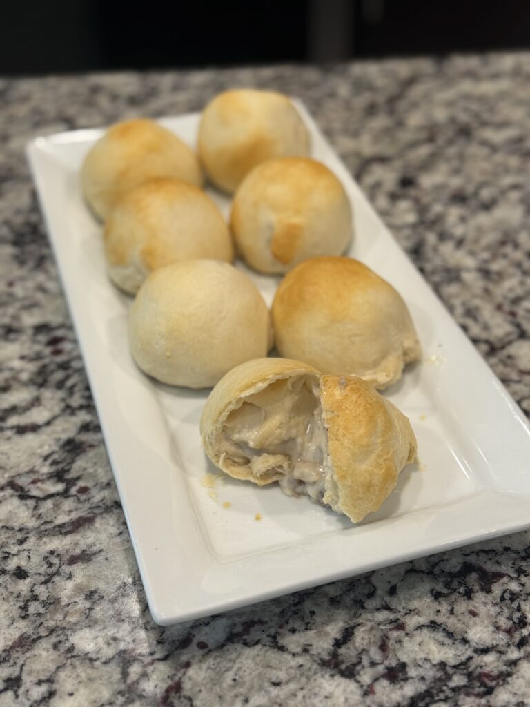 Golden biscuit bombs filled with creamy sausage gravy on a baking tray, some broken open to reveal the savory center.