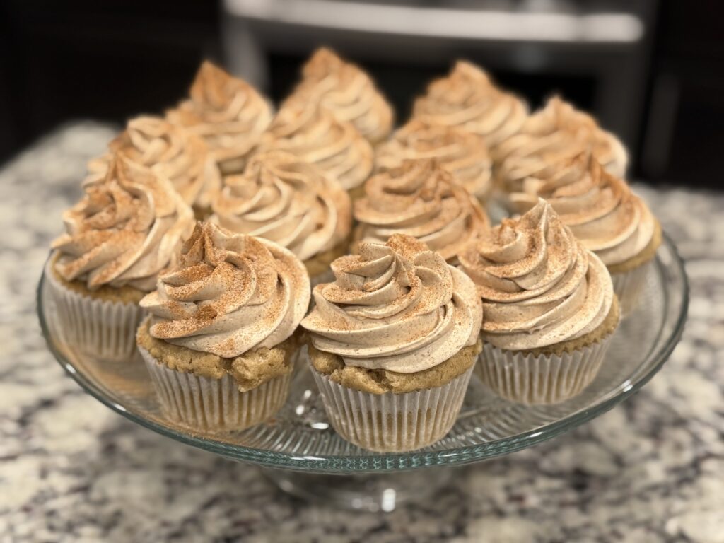 Freshly baked Snickerdoodle cupcakes with salted cinnamon frosting and cinnamon sugar topping Close-up of moist cinnamon cupcake topped with salted cinnamon frosting swirl Homemade Snickerdoodle cupcake on white plate with cinnamon sticks in background Cinnamon sugar cupcake with tall swirl of salted cinnamon frosting Teacher appreciation Snickerdoodle cupcakes on a rustic serving tray Cupcake batter in liners sprinkled with cinnamon sugar before baking Mixing bowl with creamy salted cinnamon frosting for Snickerdoodle cupcakes