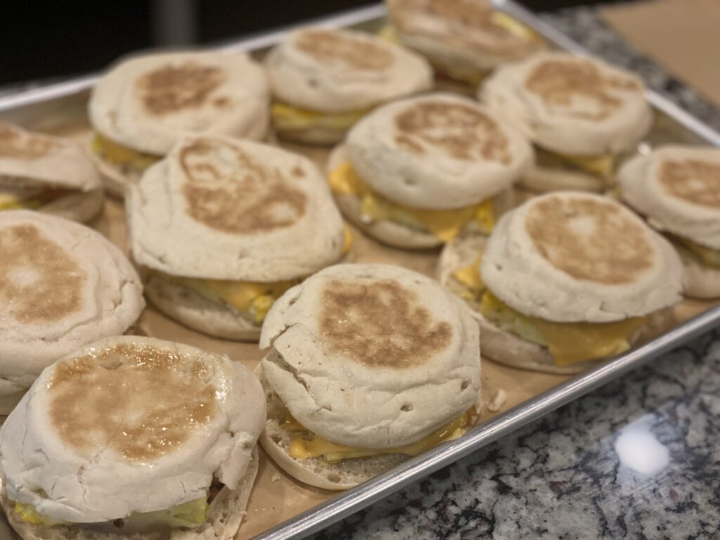 Freezer-friendly breakfast sandwiches with baked eggs, ham, and melted cheese on toasted English muffins, wrapped for easy grab-and-go mornings.