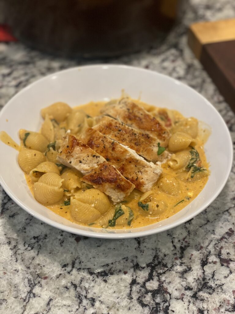 Creamy Tuscan chicken pasta served in a bowl with tender pasta shells, sun-dried tomatoes, spinach, and pan-seared chicken in a rich cream sauce, garnished with Parmesan.