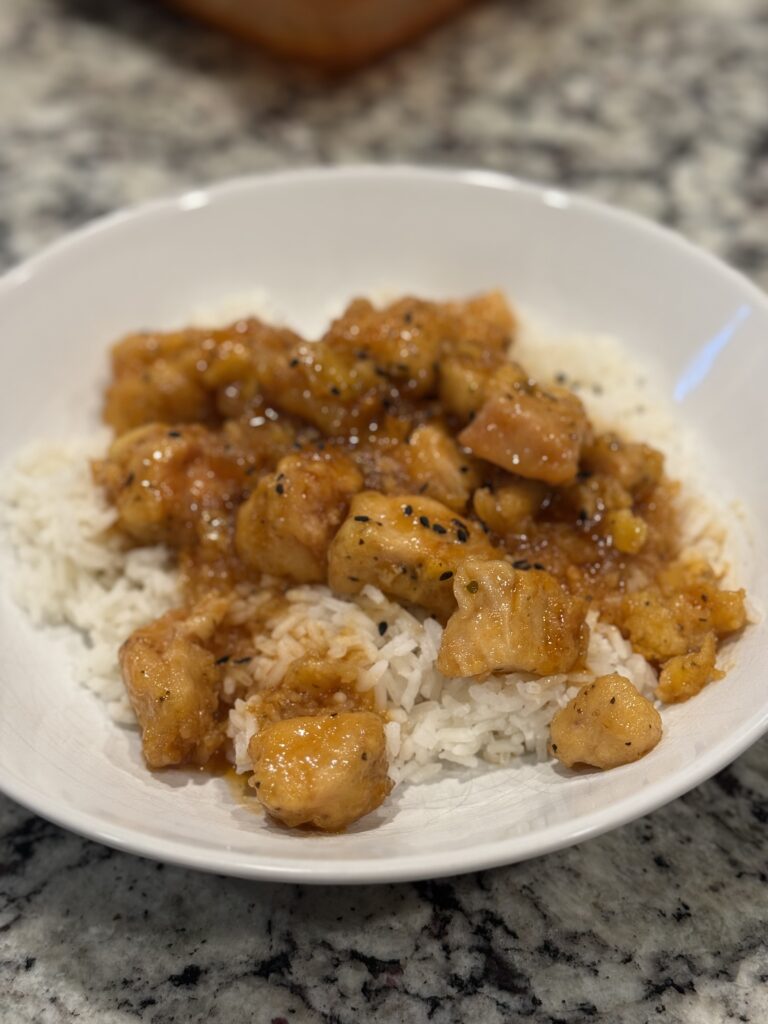 weet n sour chicken over white rice with sticky red-orange sauce — tender and glossy, not crispy.