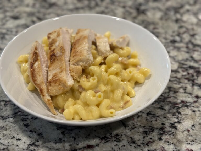 Bowl of creamy homemade macaroni and cheese with pieces of crispy bacon mixed throughout, served on a granite countertop.