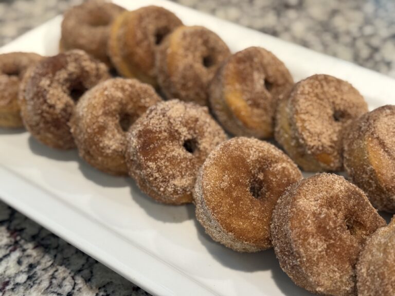 Soft golden apple cider donuts coated in cinnamon sugar arranged on a white tray