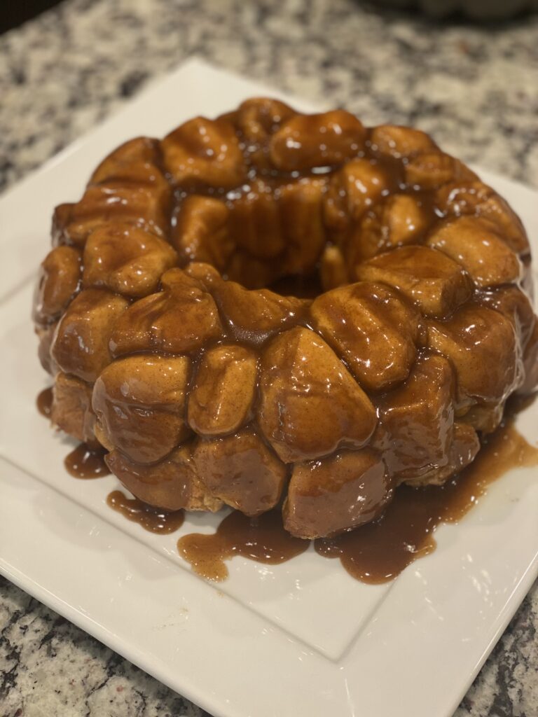 Close-up of homemade monkey bread on a white plate, covered in gooey cinnamon-caramel sauce, with soft pull-apart dough pieces glistening.