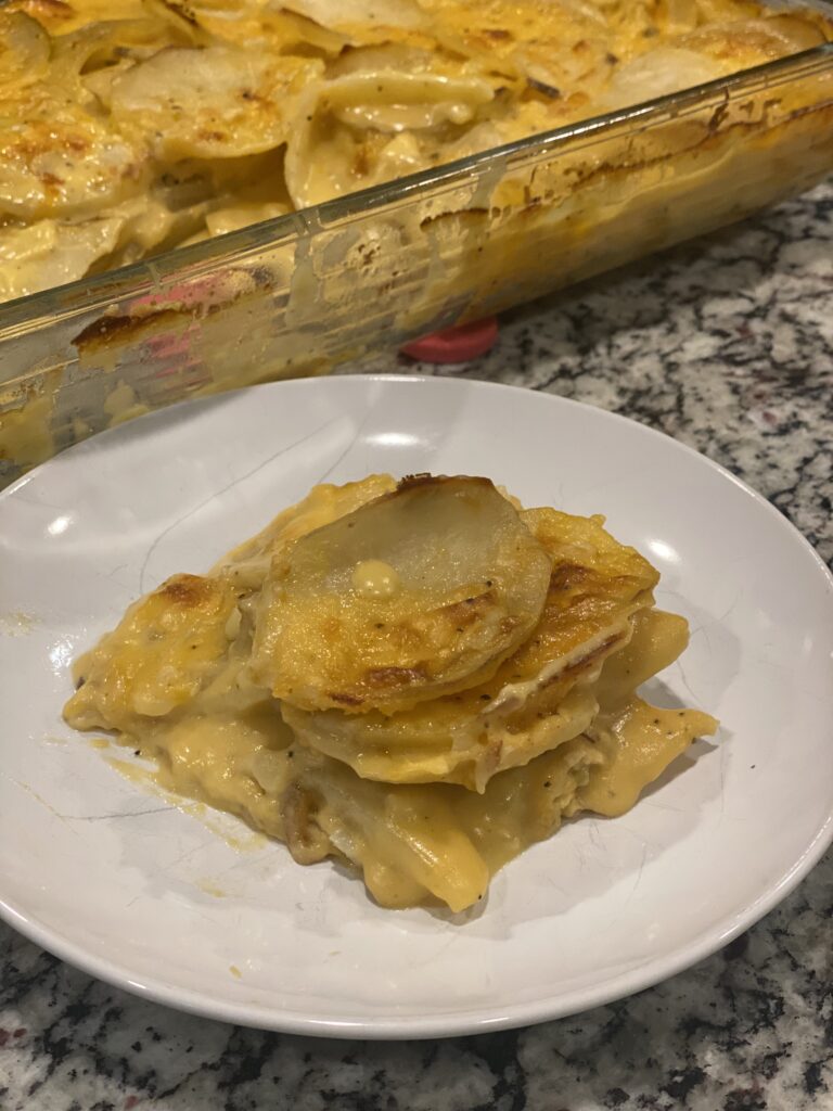 Creamy homemade scalloped potatoes served on a white plate, layered with a golden cheddar cheese sauce