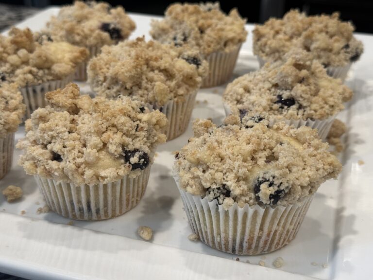 Lemon blueberry muffins topped with buttery crumb streusel on a white plate, baked with fresh blueberries and lemon zest for a moist bakery-style breakfast muffin.