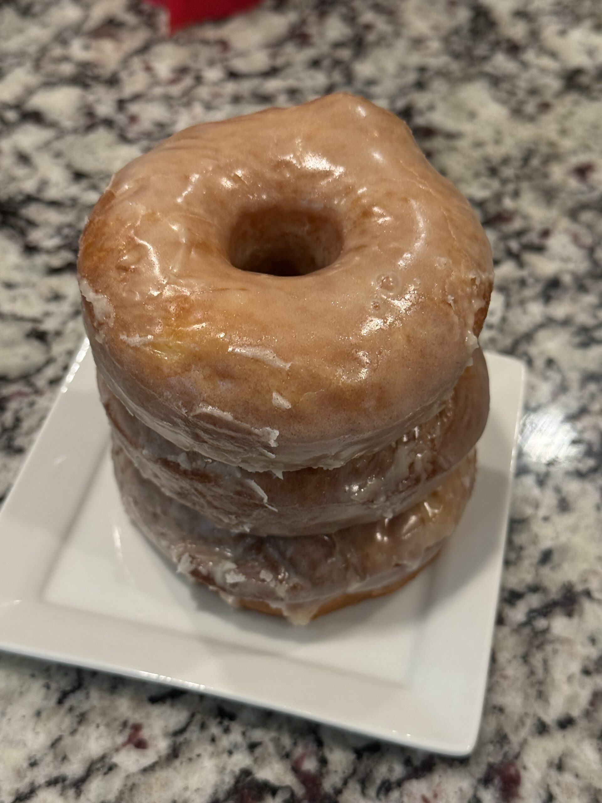 **Alt Text** Three homemade glazed donuts stacked on a white square plate. The donuts are golden brown, soft, and fluffy with a thick vanilla glaze dripping down the sides. The stack sits on a granite countertop and showcases the classic bakery-style texture and glossy glaze.