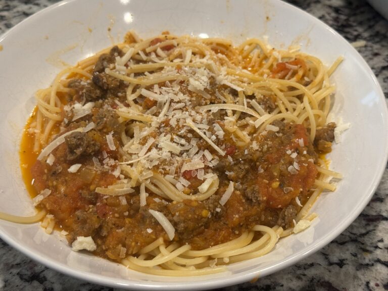 Bowl of spaghetti topped with homemade fresh tomato pasta sauce made with ground beef, onions, and chunks of fresh tomatoes, finished with grated Parmesan cheese.