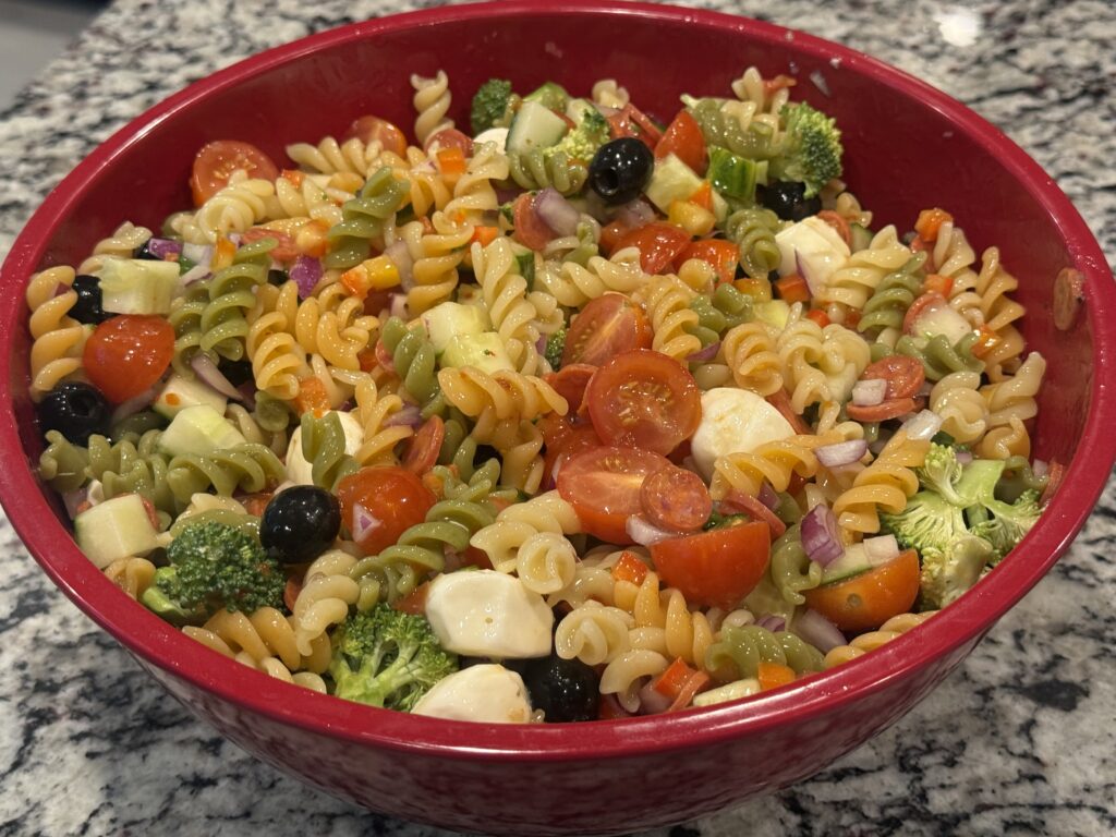 Large bowl of homemade summer pasta salad with tri-color rotini, cherry tomatoes, cucumber, broccoli, red onion, black olives, mozzarella cheese, and mini pepperoni tossed in Italian dressing.