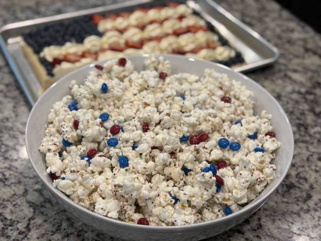 White chocolate popcorn coated with red, white, and blue M&Ms and patriotic sprinkles served in a bowl for a festive 4th of July treat.